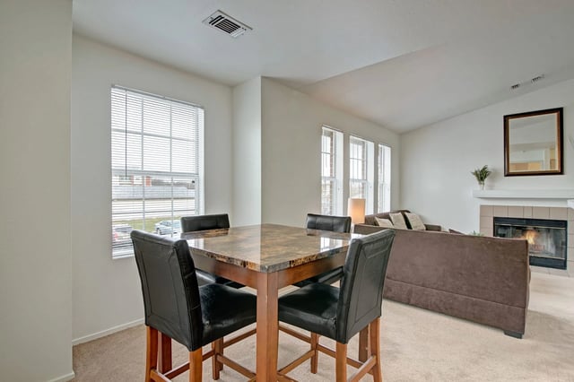 Dining area with a square table and four chairs, next to a living room with a sofa and fireplace.