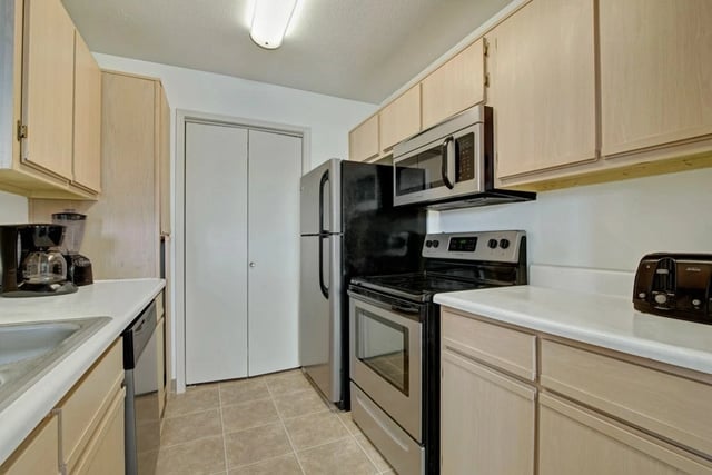 Kitchen with light wood cabinets, stainless steel appliances including refrigerator, microwave, and oven, plus a coffee maker and toaster.