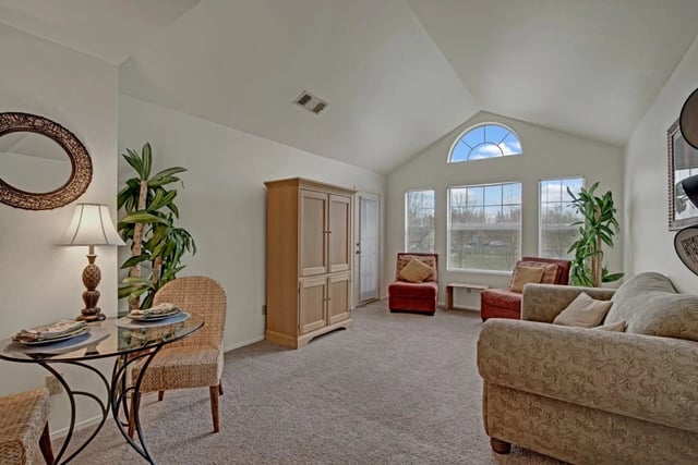 Living room with vaulted ceiling, arched window, sofa, chairs, and dining table.