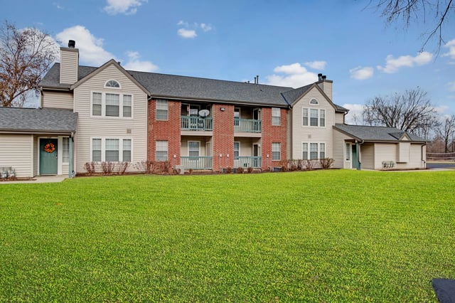 Exterior view of apartment buildings with manicured lawn and blue sky.