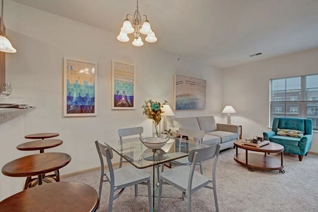Modern living and dining area with a glass-top table and chairs, a sofa, and a teal accent chair.