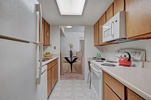 Kitchen with white appliances, wooden cabinets, and a dining area visible in the background.