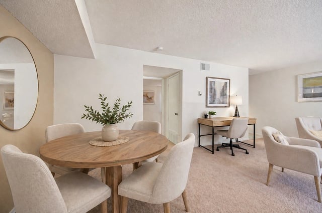 Dining area with a round wooden table and chairs, and a desk area with a computer workstation.