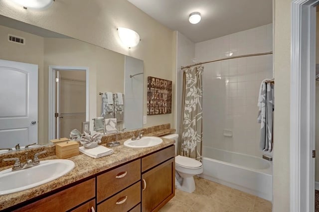 Bathroom vanity with double sinks, large mirror, tub, and toilet.