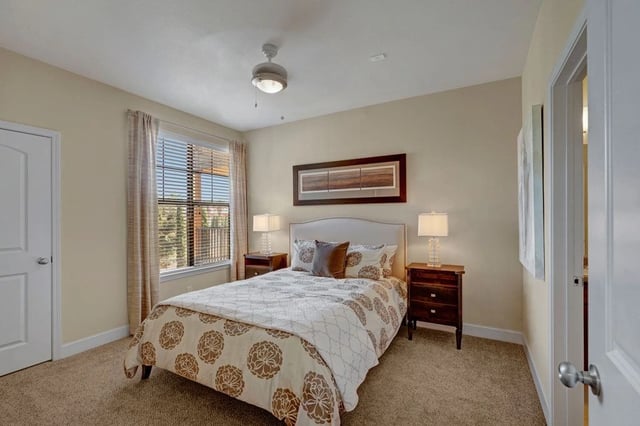 Bedroom with a queen-sized bed, nightstands, a ceiling fan, and a window with blinds.