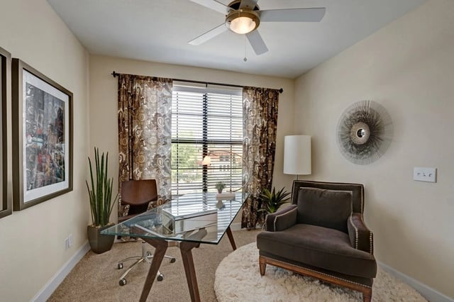 Home office with a glass desk, ergonomic chair, and comfortable armchair.