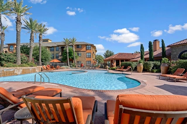 Resort-style swimming pool with lounge chairs and palm trees.