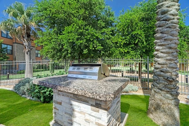 Built-in outdoor grill with granite countertop in a grassy area with trees and a palm tree.