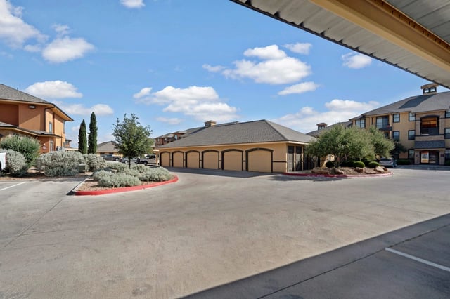 Exterior view of the apartment complex featuring buildings and a row of garages under a blue sky.