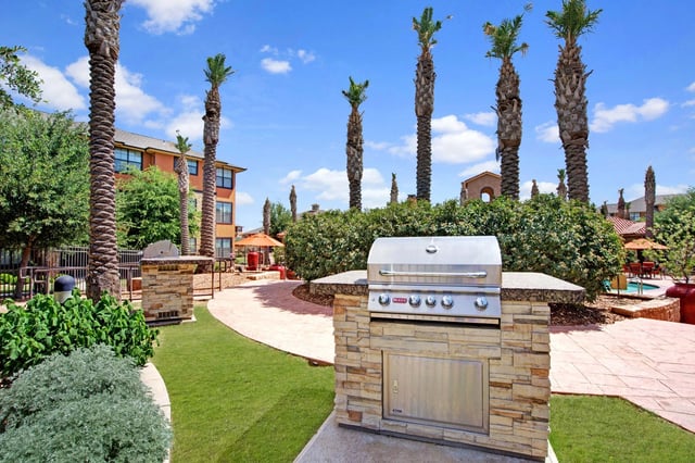 Outdoor gas grill station with a pool and seating area in the background.