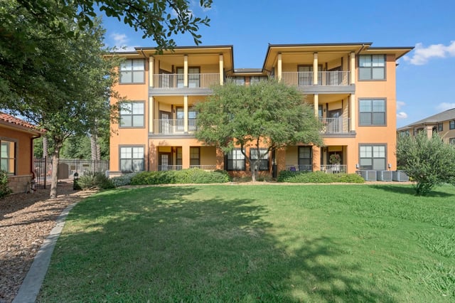 Exterior of apartment building with orange facade, balconies, and green lawn.
