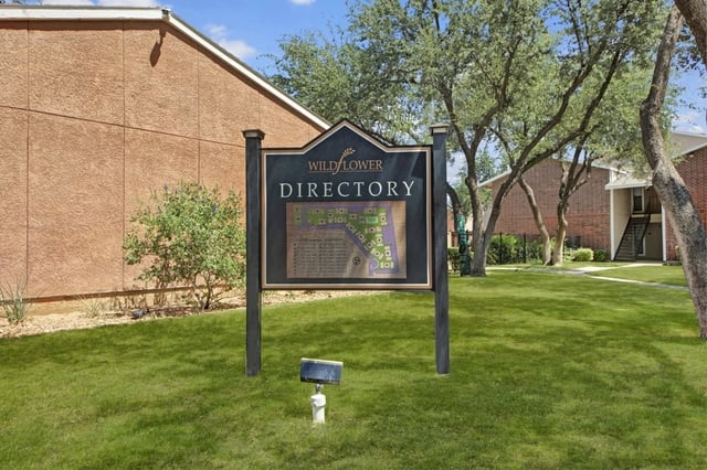 Exterior community signboard with a map at an apartment complex, surrounded by trees and grass.