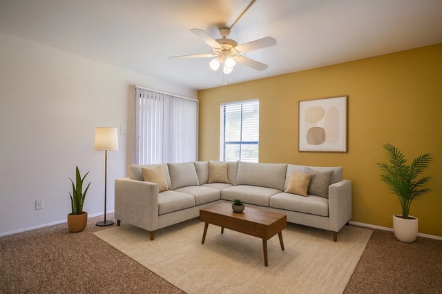 Living room with a beige sectional sofa, yellow accent wall, ceiling fan, and potted plants.