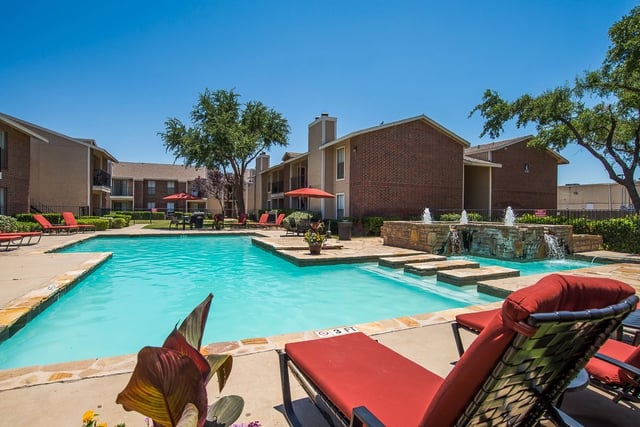 Outdoor apartment community pool with lounge chairs and umbrellas.