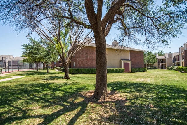 Outdoor community courtyard with grass, trees, and brick apartment buildings.