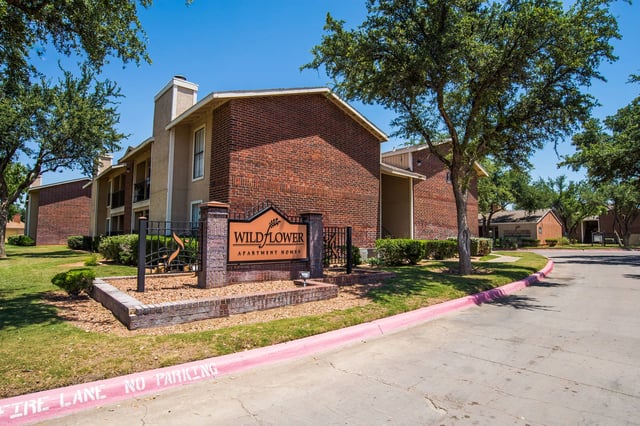 Exterior view of Wildflower Apartment Homes with brick buildings, trees, and an entrance sign.