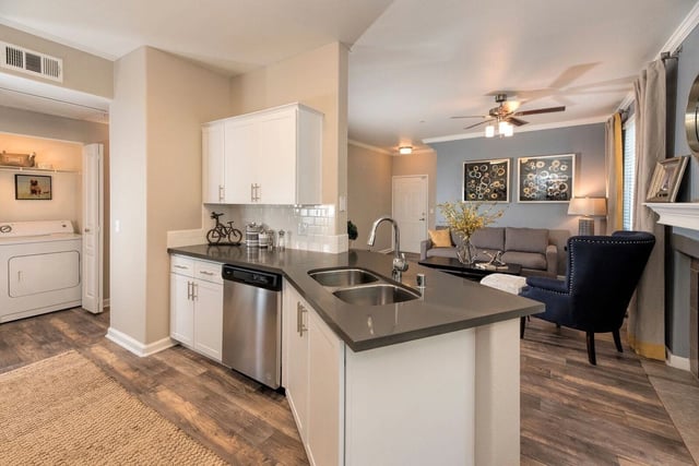 Kitchen with stainless steel appliances, a double sink, white cabinetry, and a view into the living room.