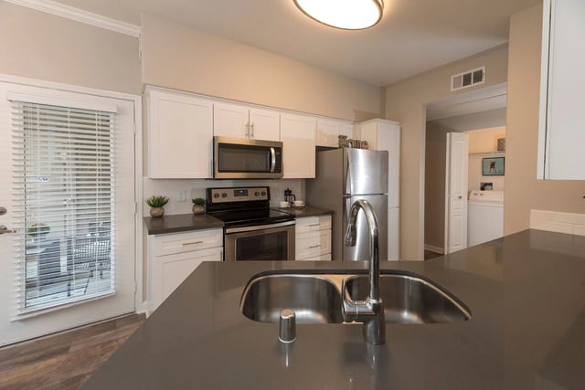 Modern kitchen with stainless steel appliances, white cabinetry, and a large island sink.