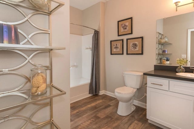 Modern bathroom with a toilet, bathtub, vanity, and decorative shelving.