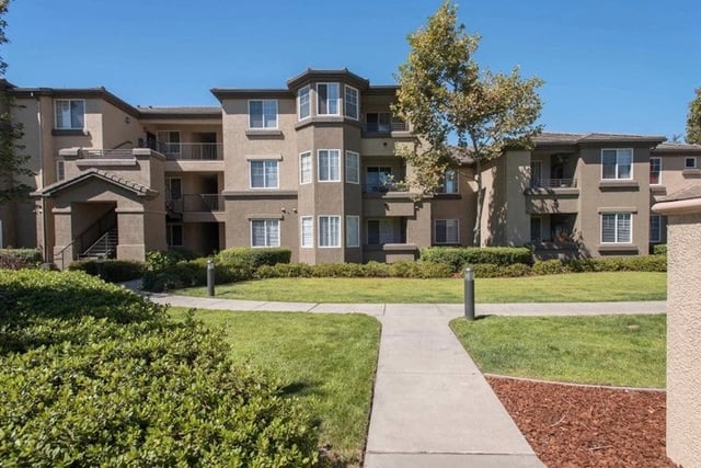 Exterior view of a multi-story apartment building with balconies and surrounding green lawn.