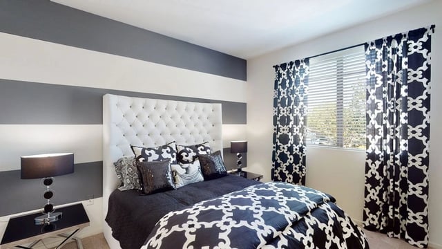 Stylish bedroom with a tufted headboard, dark bedding, and striped walls.