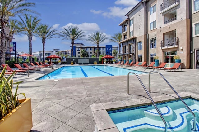 Resort-style swimming pool and hot tub with lounge chairs and palm trees.