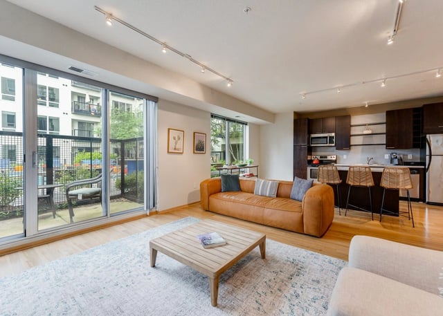 Modern living room and kitchen area with a tan sofa, coffee table, and island seating.
