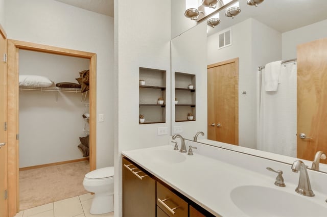 Modern bathroom with double vanity, large mirror, and walk-in closet.