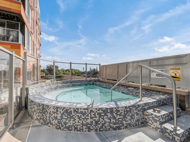 Outdoor hot tub with mosaic tile surround and steps, adjacent to a modern building.