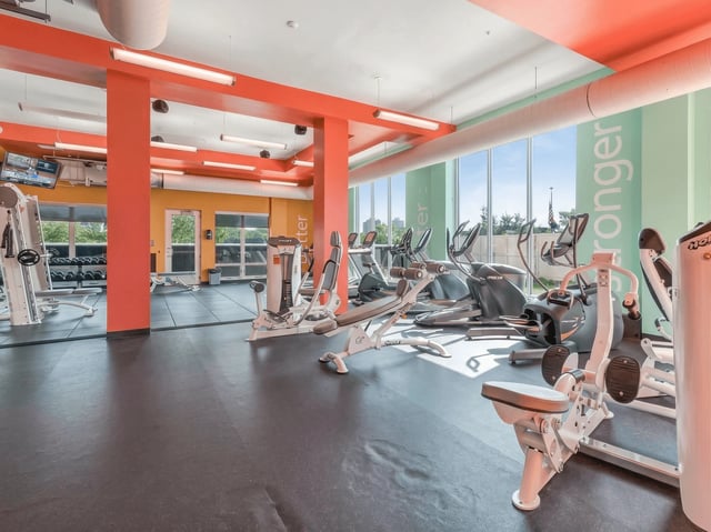 Modern fitness center with cardio machines, weight equipment, and large windows.