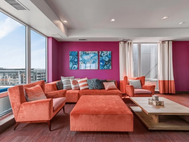 Modern communal lounge with bright orange sectional sofa, accent chairs, and artwork.