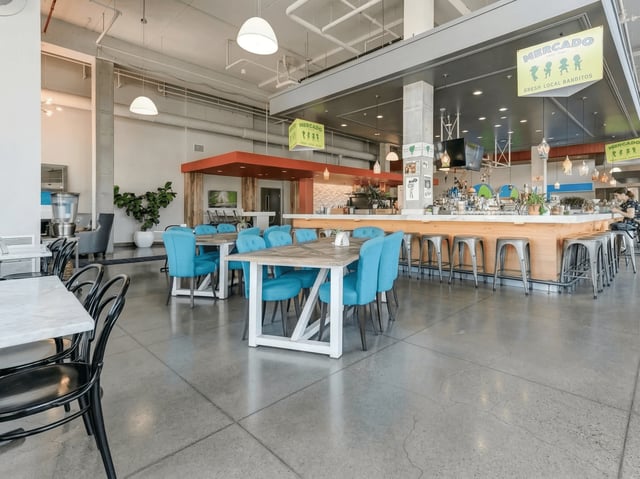 Modern communal dining area with blue chairs and tables, and a bar with stools.