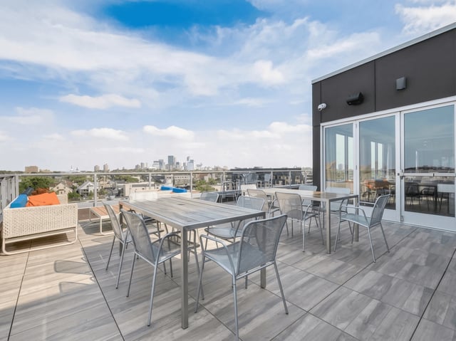 Rooftop patio with tables and chairs, overlooking a city skyline.