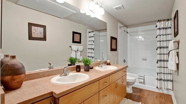 Bathroom vanity with double sinks and wood cabinets, opposite bathtub, shower, and toilet.