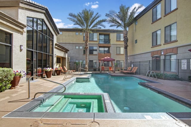 Outdoor swimming pool and jacuzzi with lounge chairs and palm trees.