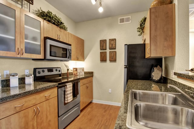 Modern kitchen with wood cabinets, granite countertops, stainless steel appliances, and a double sink.