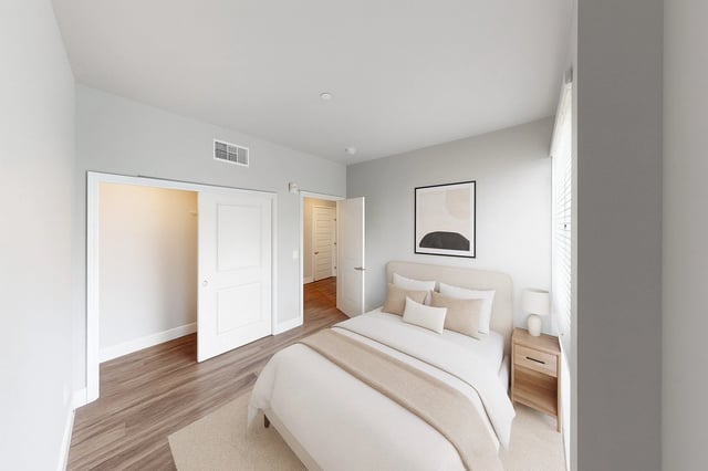 A neutral-toned bedroom with a queen-size bed, bedside table, and closet.