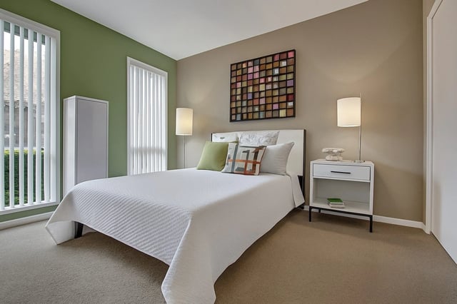 Bedroom with a queen-size bed, nightstand, and window blinds.