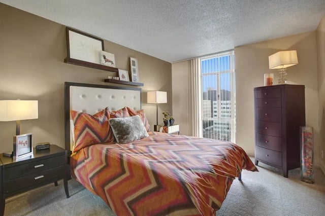 Bedroom with a king-size bed, dresser, and nightstand. Large window with blinds.