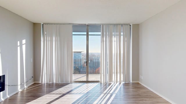 Empty living room with large sliding glass doors opening to a balcony with a view.