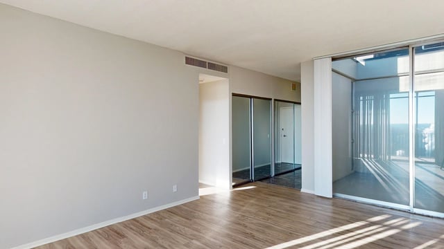 Empty living room with wood floors and large sliding glass doors leading to a balcony.