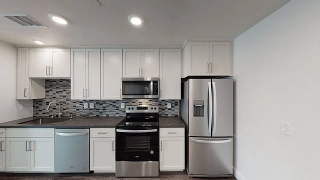Modern kitchen with stainless steel appliances, white cabinets, and a gray backsplash.