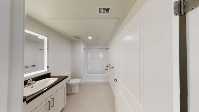 Modern bathroom with vanity, illuminated mirror, toilet, and bathtub.