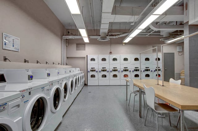 On-site laundry room with rows of washers and dryers, plus a communal table and chairs.
