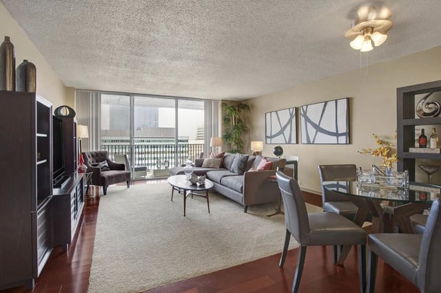 Spacious living room with a large sectional sofa, coffee table, and dining area, featuring large windows with city views.