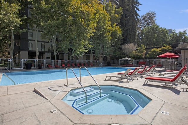 Outdoor swimming pool and hot tub with lounge chairs and red umbrellas.