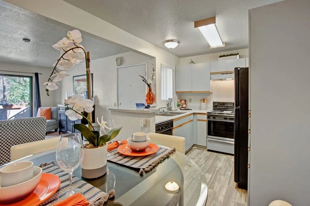 Dining area and kitchen with white cabinets, black appliances, and a round glass dining table with place settings.