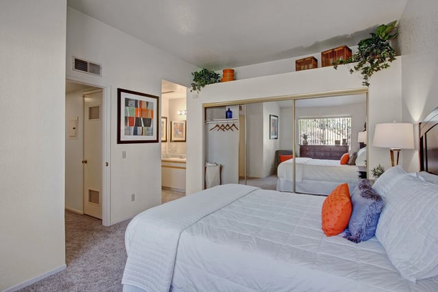 Spacious bedroom with a king-size bed, mirrored closet doors reflecting another bed, and a doorway to the bathroom.
