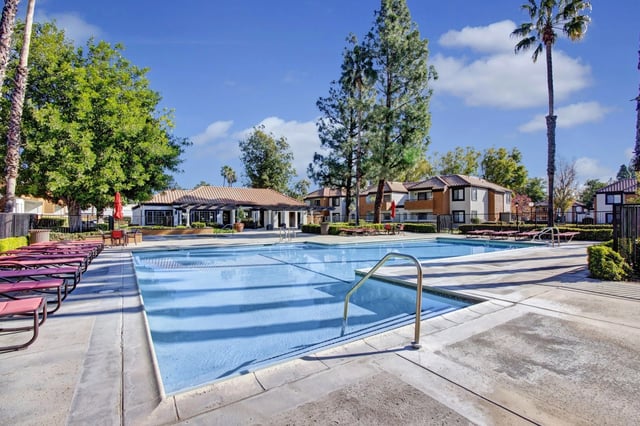 A sparkling blue swimming pool with lounge chairs and umbrellas, adjacent to apartment buildings on a sunny day.