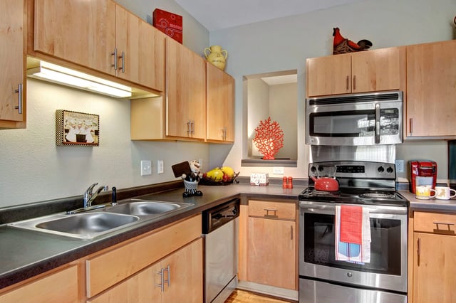 Modern apartment kitchen with light wood cabinets, stainless steel stove and sink.